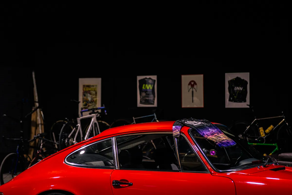 Bikes and framed team jerseys on the shop floor, behind a red classic car.